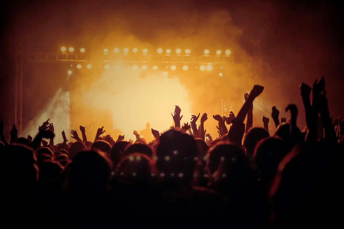 Crowd with raised hands in front of a warmly lit main stage