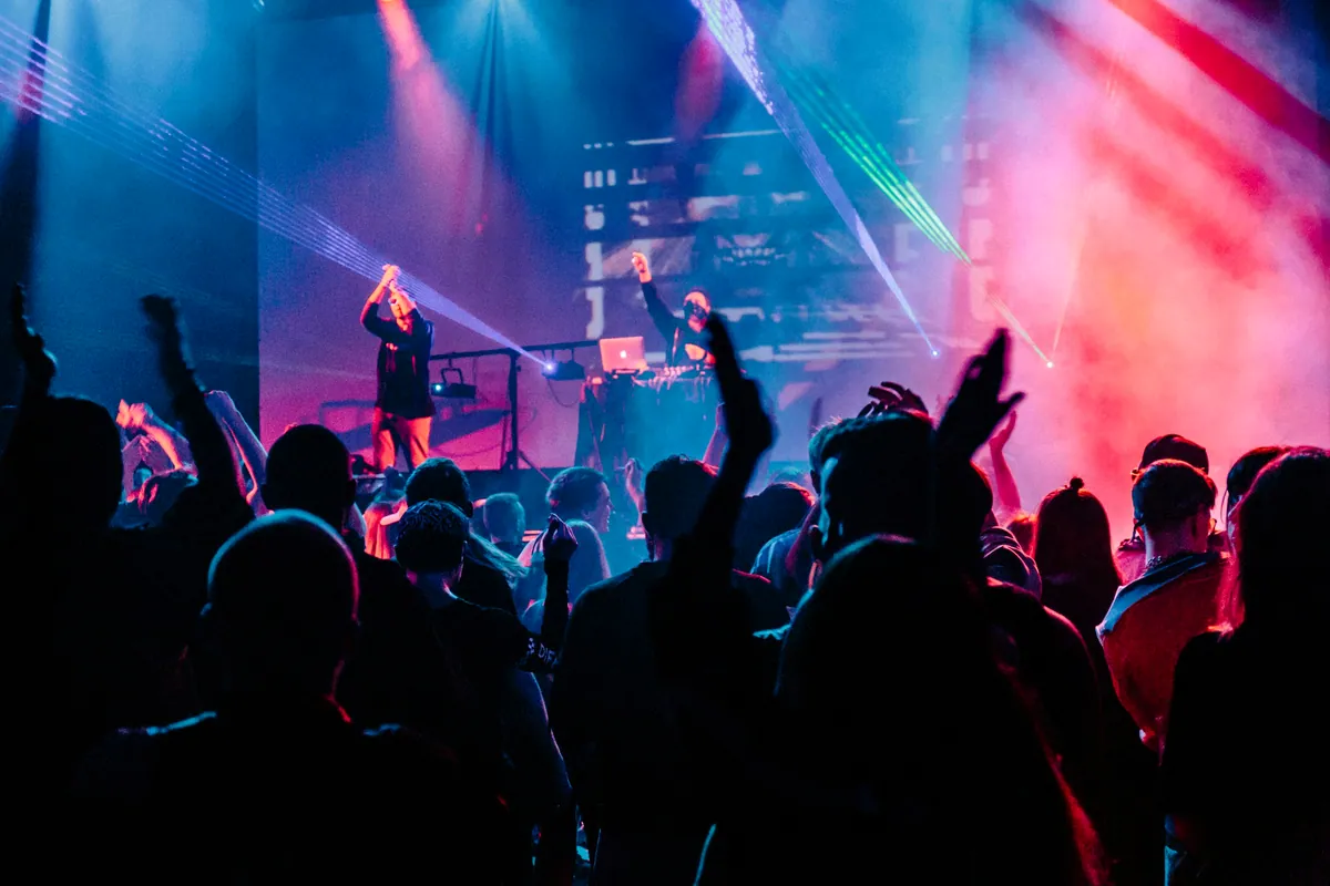 Crowd with hands raised under stage lights at an open-air night club